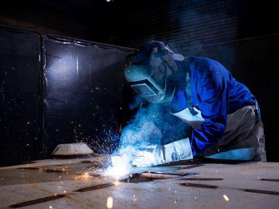 Eine computergesteuerte Laserschneidanlage bearbeitet eine dicke Stahlplatte in der Stapu-Werkhalle. Der helle Lichtpunkt des Lasers und der präzise Schnittverlauf verdeutlichen die moderne Technik bei der Formgebung schwerer Bauteile.