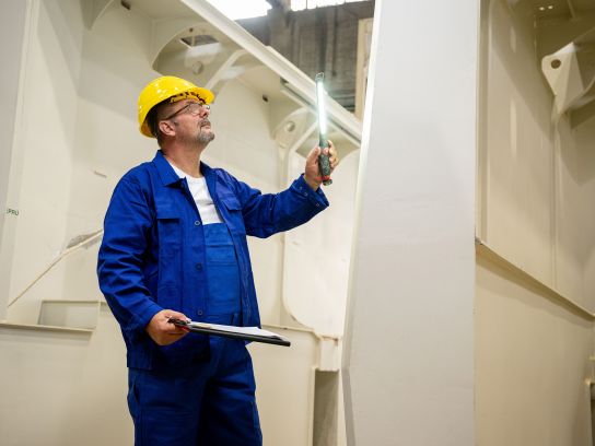 Ein Mitarbeiter der Stapu GmbH & Co. KG prüft mit einem präzisen Messwerkzeug die Maße eines massiven Stahlbauteils. Die sorgfältige Kontrolle stellt sicher, dass jedes Gegengewicht exakt den Kundenvorgaben und Sicherheitsstandards entspricht.