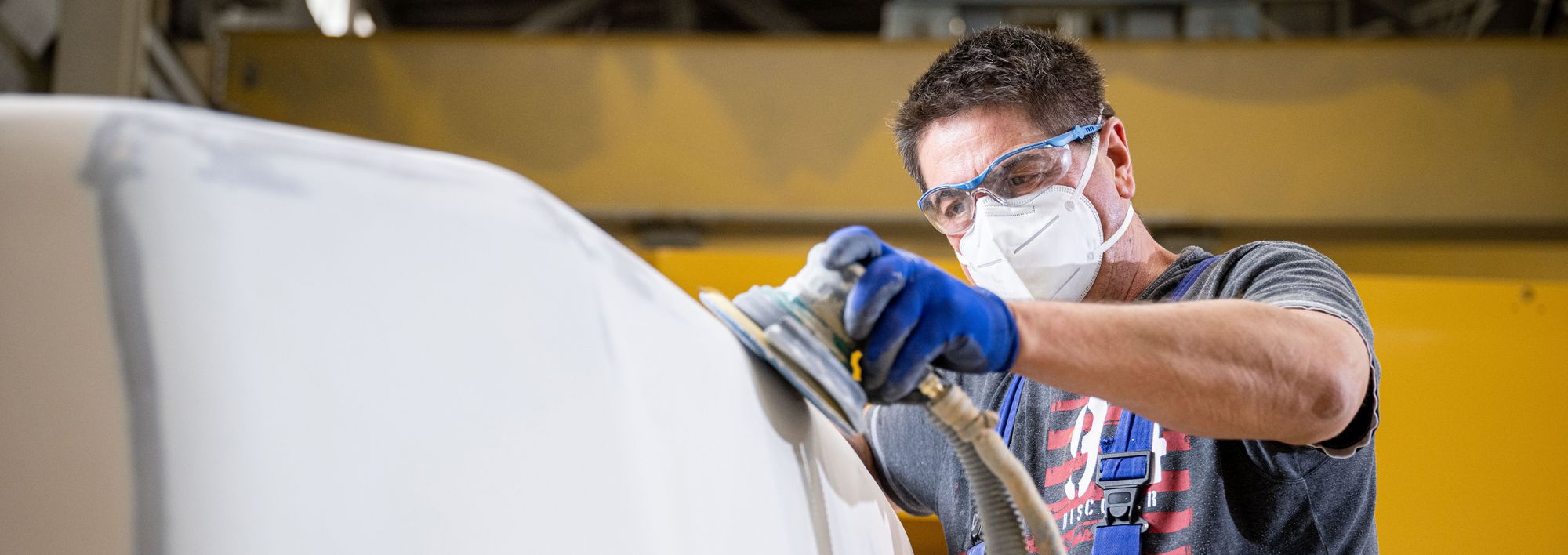 Fachkraft mit Schutzausrüstung bei Schleifarbeiten an einem großen Bauteil in der Produktion.