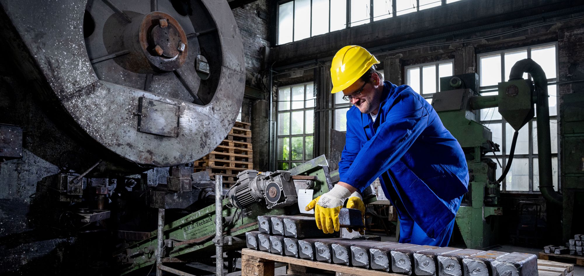 Industrielle Stahlbearbeitung durch einen qualifizierten Mitarbeiter beim Stapeln von exakt zugeschnittenen Stahlknüppeln auf einer Europalette.
